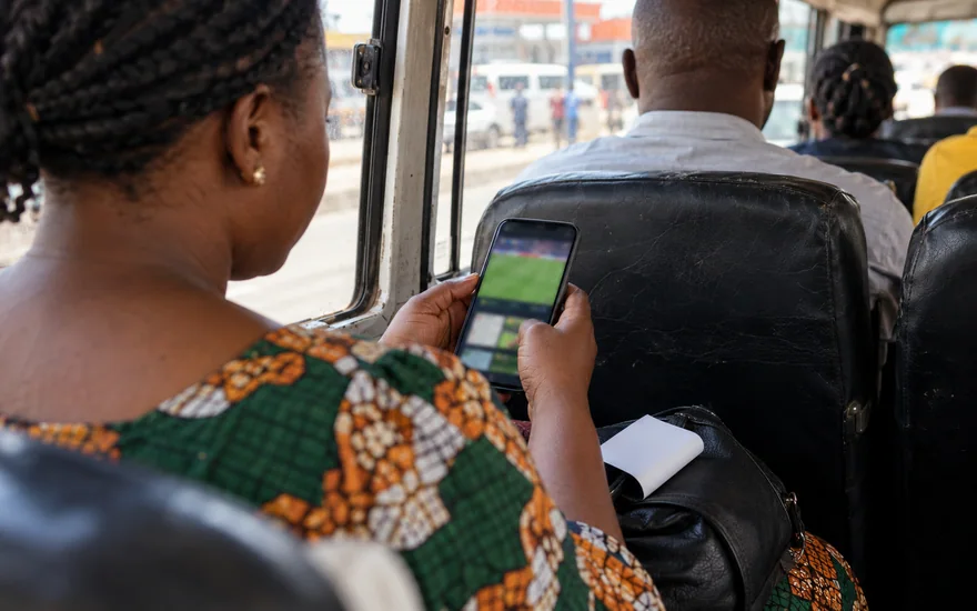 betPawa app mobile access with a Zambian adult comparing two blurred betting phone screens beside an unreadable printed bet slip