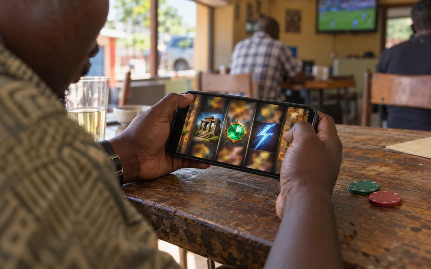 Best slots Zambia scene with temple, gem and lightning-themed reels on a blurred phone beside unmarked chips.