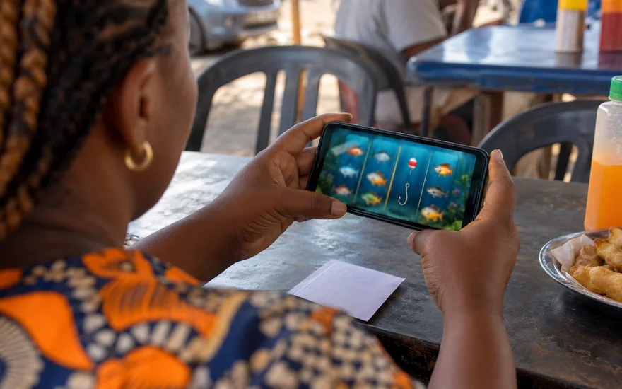 Best slots Zambia illustrated by a local adult viewing fishing-themed phone reels beside a blank betting coupon.