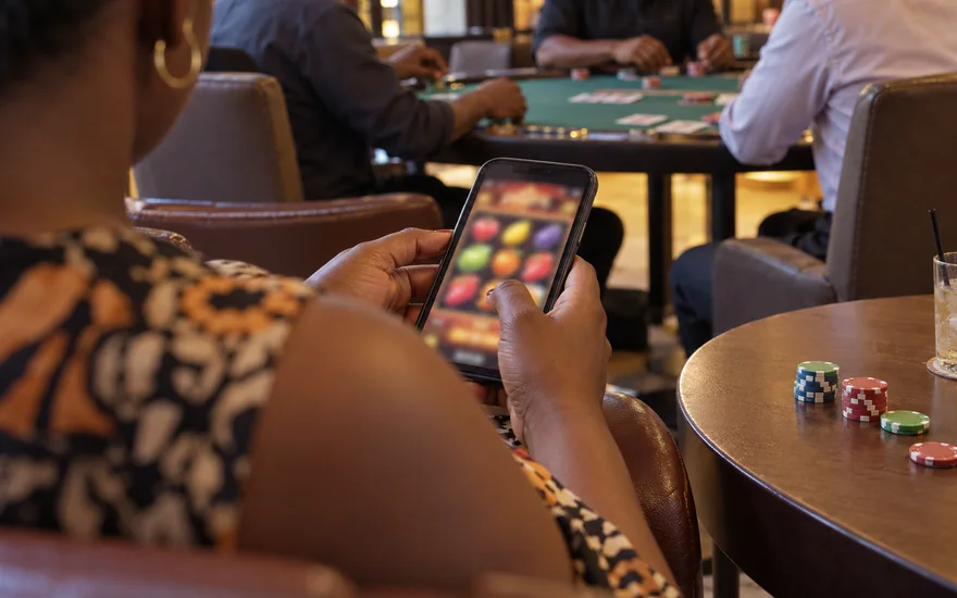 betPawa casino scene with a Zambia adult using a blurred slot phone near a card table.