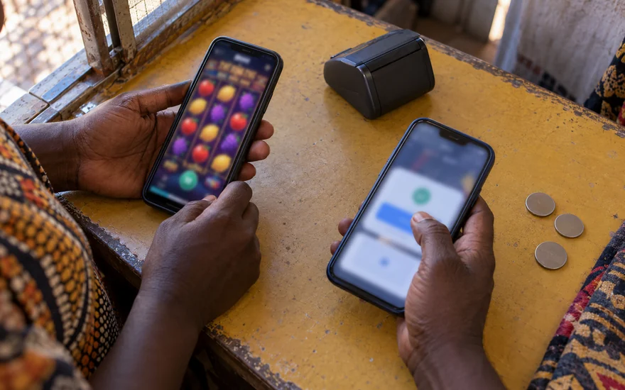 Mobile money casino Zambia comparison with casino and wallet phones beside an agent terminal on a yellow counter.
