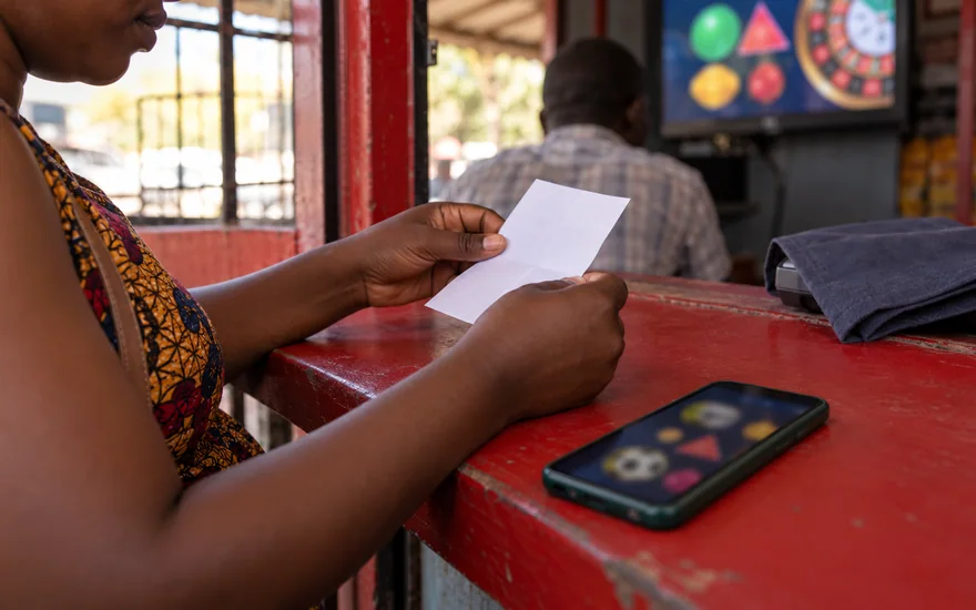 betPawa promo code offer preparation with a calculator, indistinct kwacha notes and a betting phone at a Lusaka payment counter
