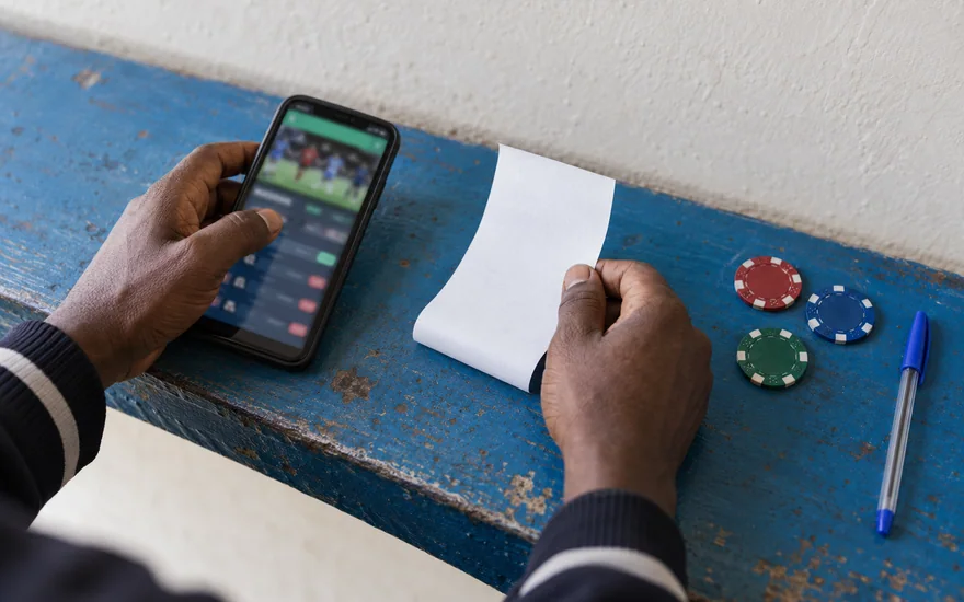 betPawa customer care security scene showing a hand covering a phone with a blurred sportsbook screen beside an unreadable SIM card holder.