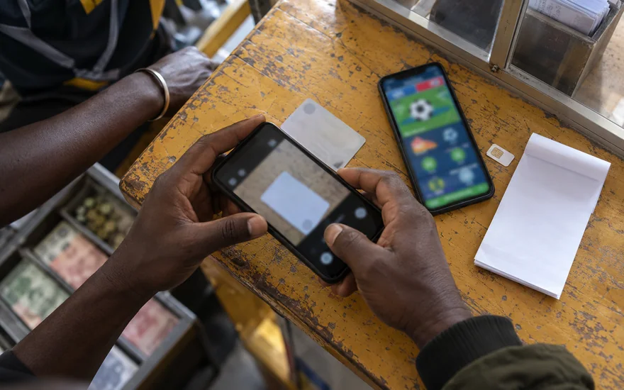 betPawa verification preparation with an unreadable Zambian identity card beside a phone showing a blurred betting account screen.