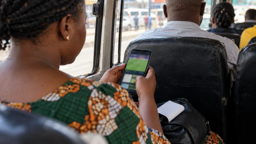 betPawa app mobile access with a Zambian adult comparing two blurred betting phone screens beside an unreadable printed bet slip