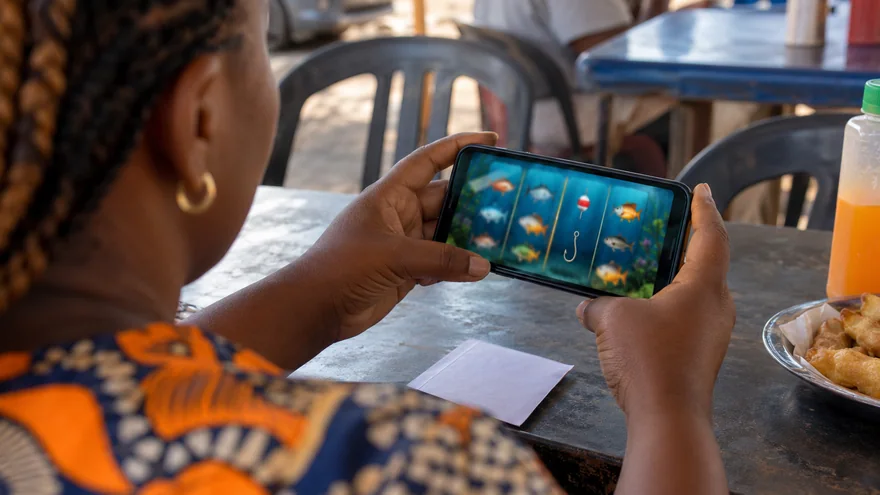 Best slots Zambia illustrated by a local adult viewing fishing-themed phone reels beside a blank betting coupon.