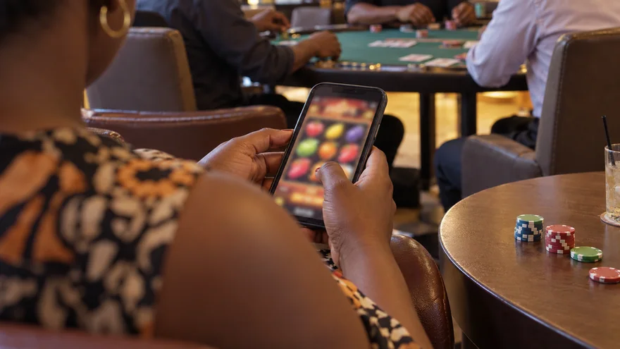 betPawa casino scene with a Zambia adult using a blurred slot phone near a card table.