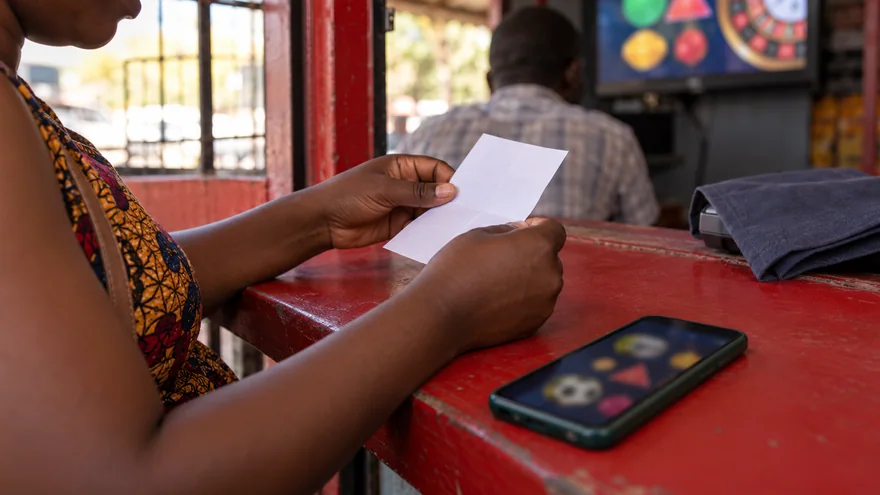 betPawa promo code offer preparation with a calculator, indistinct kwacha notes and a betting phone at a Lusaka payment counter