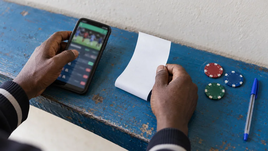 betPawa customer care security scene showing a hand covering a phone with a blurred sportsbook screen beside an unreadable SIM card holder.